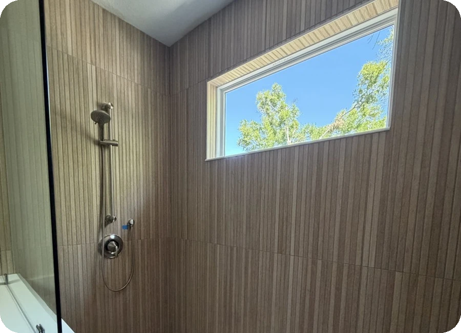 Wood-look large format porcelain tile shower with penny mosaic floor and natural light window